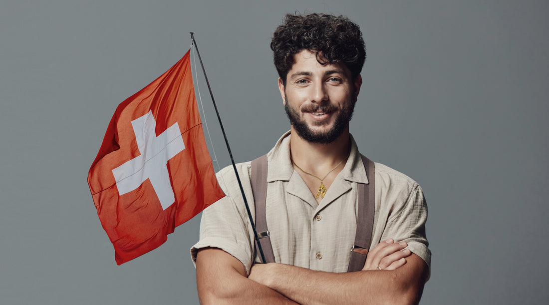 Ein junger Mann, gekleidet in traditionelle Tracht mit Lederhose und einer Schweizer Flagge in der Hand, repräsentiert den vielseitigen Motivschmuck von Rhomberg.